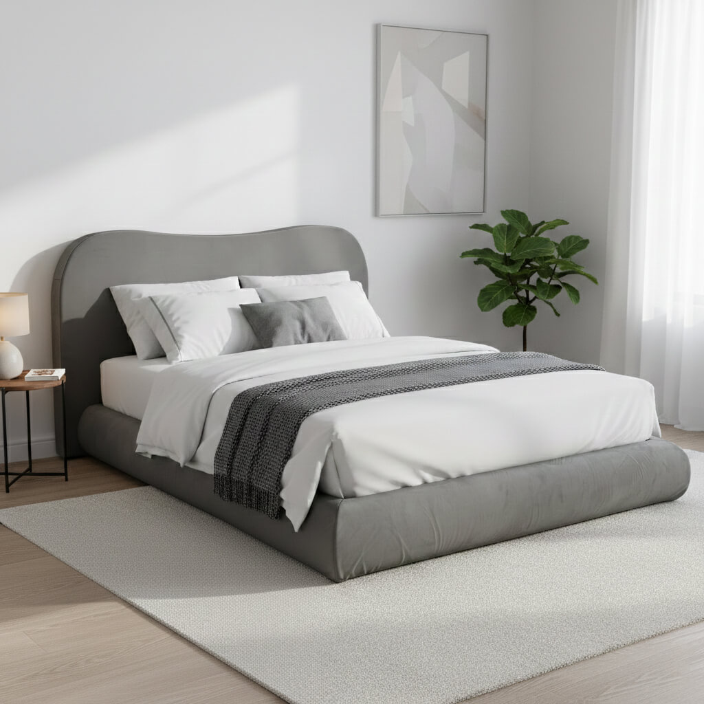 Modern minimalist gray upholstered platform bed with a camelback headboard, styled in a bright, sunlit bedroom with white bedding and a green plant