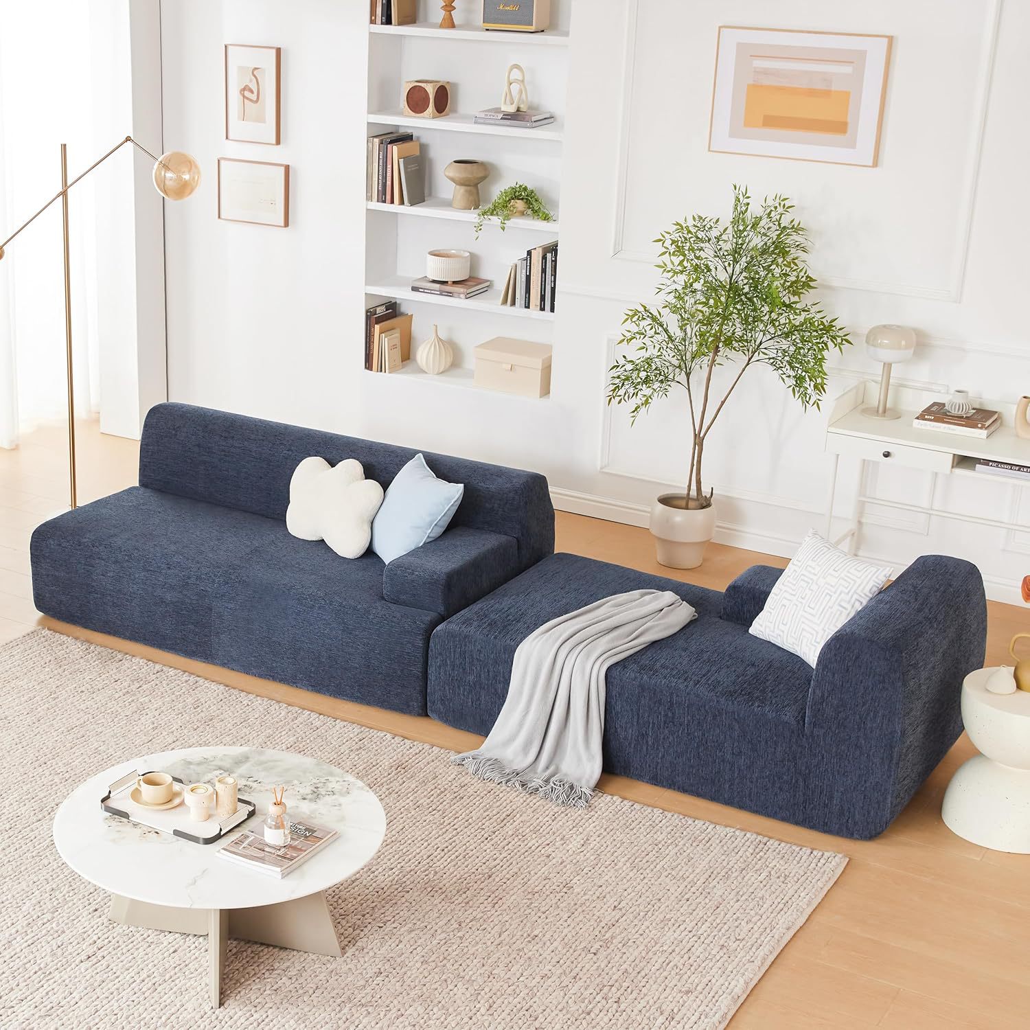 Elevated overhead view of a navy blue chenille L-shaped sectional sofa slipcover in a modern living room, featuring a marble coffee table, cream woven rug, and minimalist white bookshelf decor.