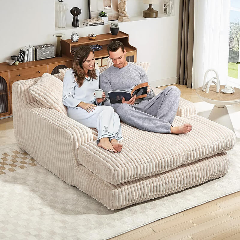 A young couple sitting on a large, soft cream corduroy floor sofa in a modern living room